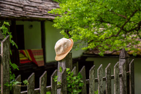 A yellow straw lady hat resting on a fence post with farmland in the background in Bulgarian village.の写真素材