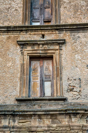 Closeup of a wooden frame window on ancient house in a village. A small window and grey stone or brick wall of an old antique building in Italy.の写真素材