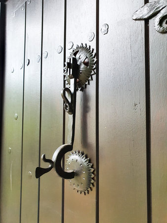 Close-up of a vintage iron door handle and decorative rosettes mounted on a painted wooden plank...