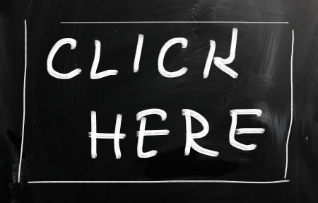 "Click here" handwritten with white chalk on a blackboardの写真素材