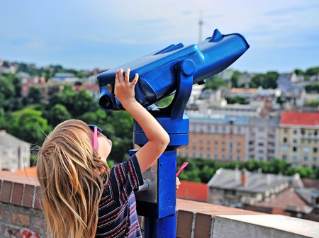 Little traveler trying to use coin-operated binoculars to see the city skylineの写真素材