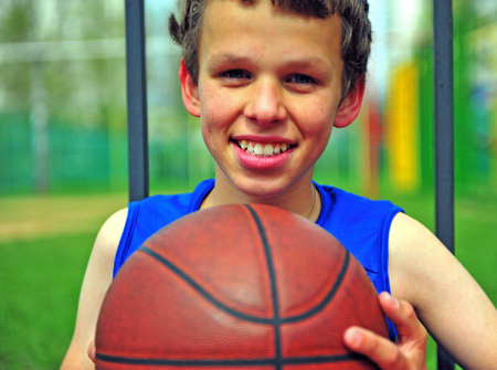 Smiling boy with a basketball on the court, summer outdoor sceneの写真素材