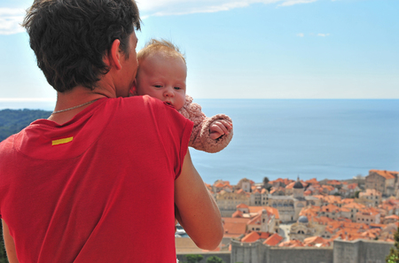 Young man with a baby looking at Dubrovnik old town from aboveの写真素材