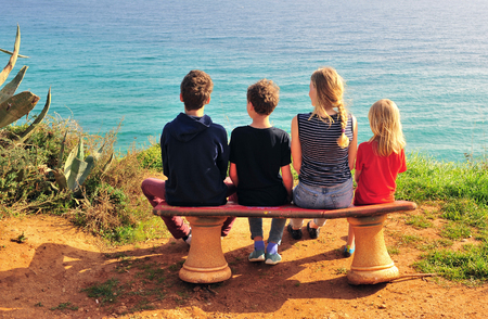 Back view of family of four sitting on beach over the seaの写真素材