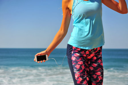 Active girl with smartphone and headphones standing on beach