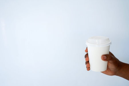 The hand of a dark-skinned man holds a disposable cup for coffee