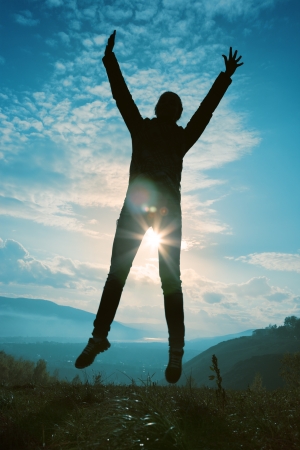 Silhouette of happy young woman jumping at the sunset の写真素材