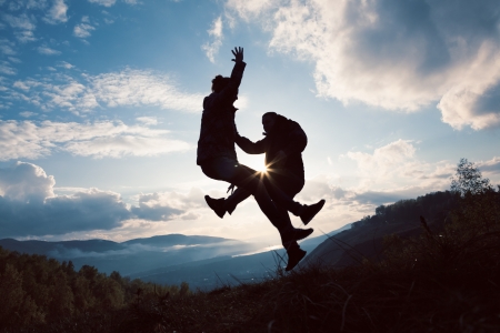 silhouettes young woman and man jumping at the sunset の写真素材