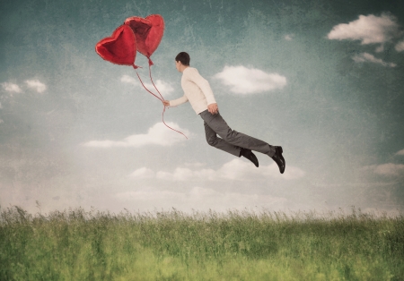 The young  man flying by a balloon in the form of heartの写真素材