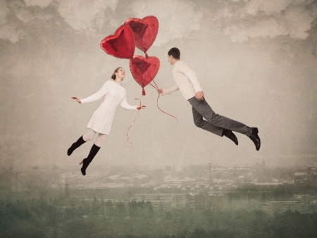 The young woman and the man flying by a balloon in the form of heartの写真素材