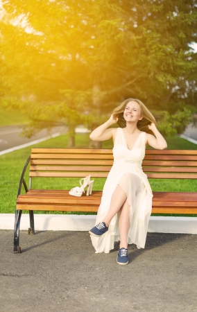 gorgeous girl sitting on a bench, laughing and a smiling,  has changed footwear on a high heel for convenient slippersの写真素材
