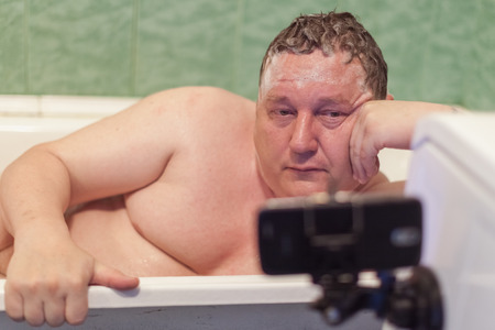 Man in bathroom looking in the smartphone, it shall cleave to the washing machineの写真素材