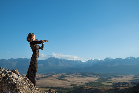 Girl in concert dress, playing the violin, standing on top of a mountainの写真素材