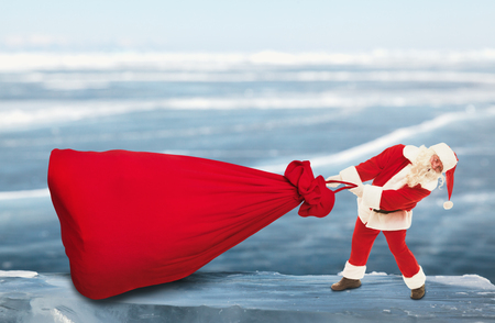 Santa Claus pulls big red bag on the frozen lake in winterの写真素材