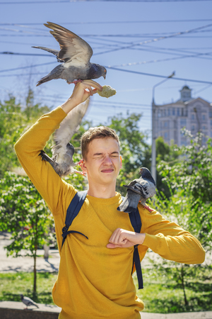 Teen boy feeds pigeons on city street summer dayの写真素材