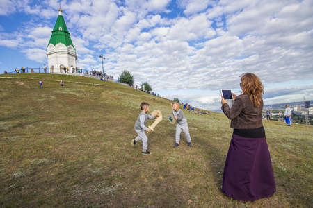 Krasnoyarsk, Russia - September 03 2016: Mom takes on the tablet as a fight with swords of her children on the food festival "Summer Kitchen"  on the mountain Pokrovskayaのeditorial素材