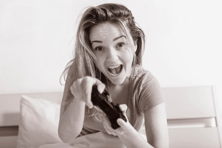 Girl teen playing console sitting up in bed, black and white photo