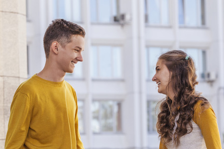 A guy and a girl are smiling, looking at each other on a city streetの写真素材