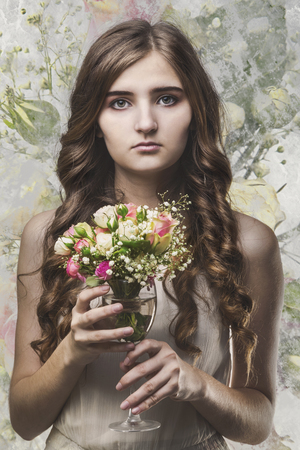 Girl with long hair and bouquet of flowers in a glass looks at the camera の写真素材