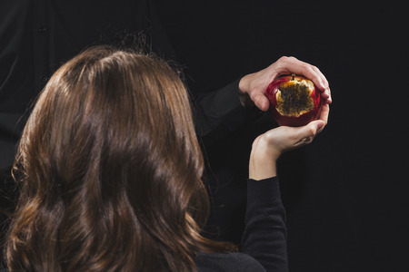 Rotten apple of knowledge, a young girl gives it to a man on a black backgroundの写真素材