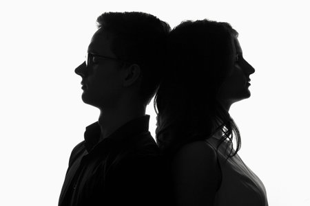 silhouette of a couple, a young girl and a guy leaned against each other nape against a white backgroundの写真素材