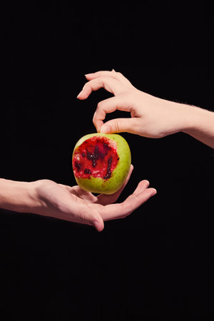 Woman offers  bloody apple to a man,  symbol of dangerous knowledge, close-up, hands