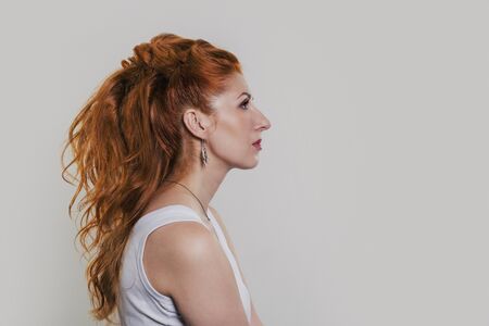 Studio portrait of a young beautiful red-haired woman in a white T-shirt in gentle colors in profileの写真素材