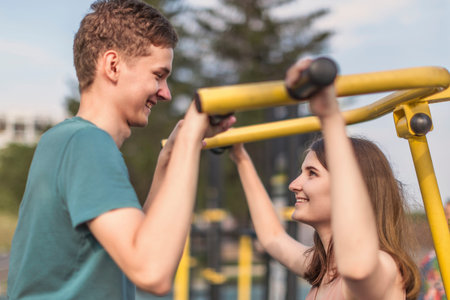 Gym on the street: Young man and girl shakes muscles on a street public fitness machine
