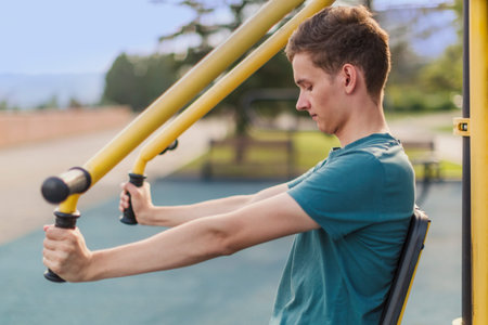 Gym on the street: Young man shakes muscles on a street public fitness machine
