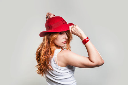 Young red-haired woman in a white tank top and red hat. Studio photo