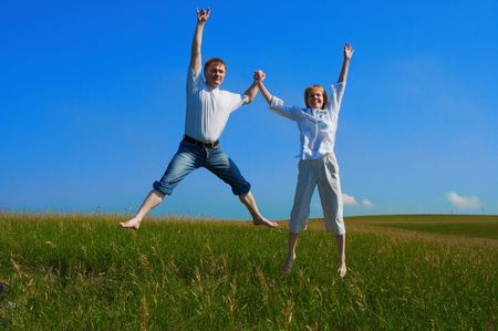 couple jumping in field under blue skyの写真素材