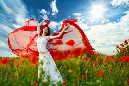 beauty woman in poppy field with red tissue under skyの写真素材