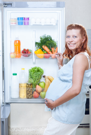 pregnant woman and refrigerator with health food vegetables and fruitsの写真素材