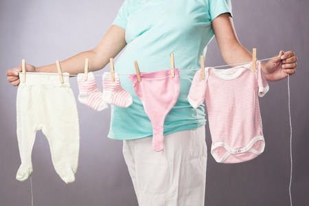 pregnant woman with rope pins baby clothes on gray backgroundの写真素材