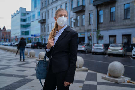 Business woman in a black suit and a mask on her face to protect herself from the virus walks around the cityの写真素材