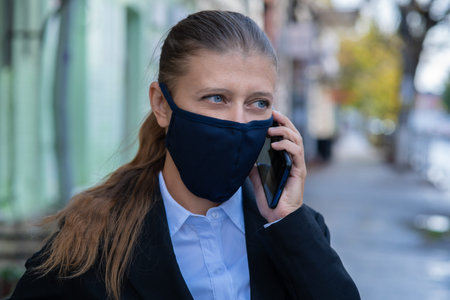 Business woman in a black suit and a mask on her face to protect herself from the virus walks around...