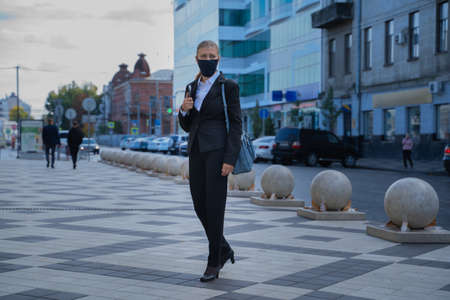 Business woman in a black suit and a mask on her face to protect herself from the virus walks around the cityの写真素材