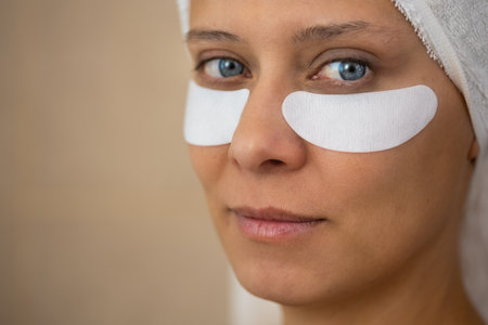 Adult beautiful woman in the bathroom and a towel takes care of her skin and applies eye patches to her faceの写真素材
