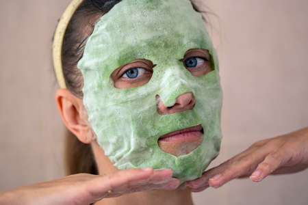 Adult beautiful woman in a bathroom and a towel takes care of her skin applies a green tissue wellness face maskの写真素材