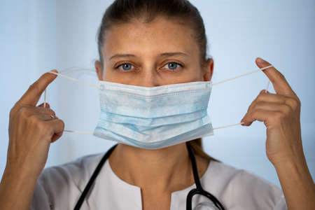 Medical doctor woman in special medical clothes in a protective mask on her face from coronavirus and a stethoscope around her neckの写真素材