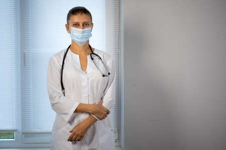Medical doctor woman in special medical clothes in a protective mask on her face from coronavirus and a stethoscope around her neckの写真素材