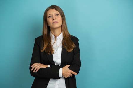 Beautiful Adult Business Woman In Black Suit And White Shirt Stands With Arms Crossed On Her Chest On A Blueの写真素材