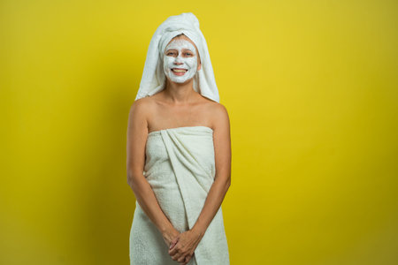 Beautiful woman wrapped in a towel with anti-wrinkle skin cream puts on a mask on her face on a...