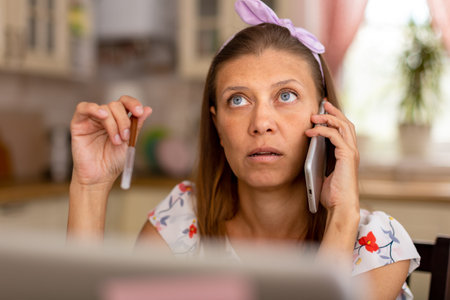 Beautiful adult woman at home in the kitchen working on a laptop and uses a smartphone