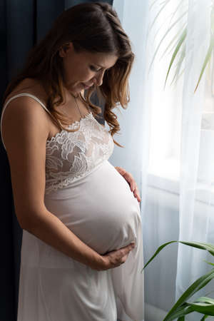 Pregnant Woman Lying On Bed At Home And Stroking Her Big Belly While Awaiting Baby's Birthの写真素材