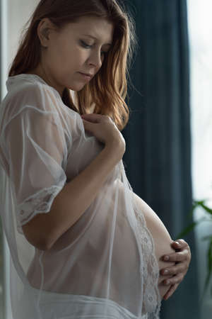 Pregnant Woman Lying On Bed At Home And Stroking Her Big Belly While Awaiting Baby's Birthの写真素材