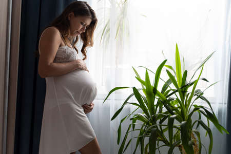 Pregnant Woman Lying On Bed At Home And Stroking Her Big Belly While Awaiting Baby's Birthの写真素材