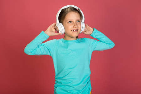 Little Beautiful Baby Girl Pink Background Bright Clothes Yellow Pants Turquoise Blue Shirt Wearing White Headphones Listening To Music And Danceの写真素材