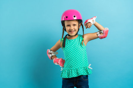 Little girl child in protective clothing helmet knee pads elbow pads with rollers on a blue...