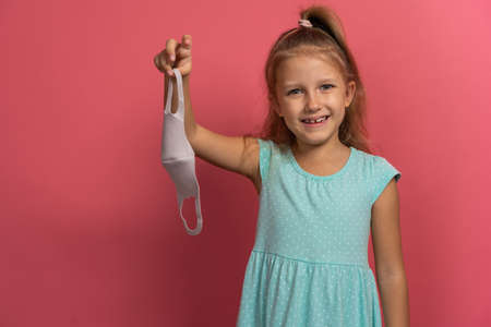 Little beautiful child girl in blue dress take off face mask and smile on pink backgroundの写真素材